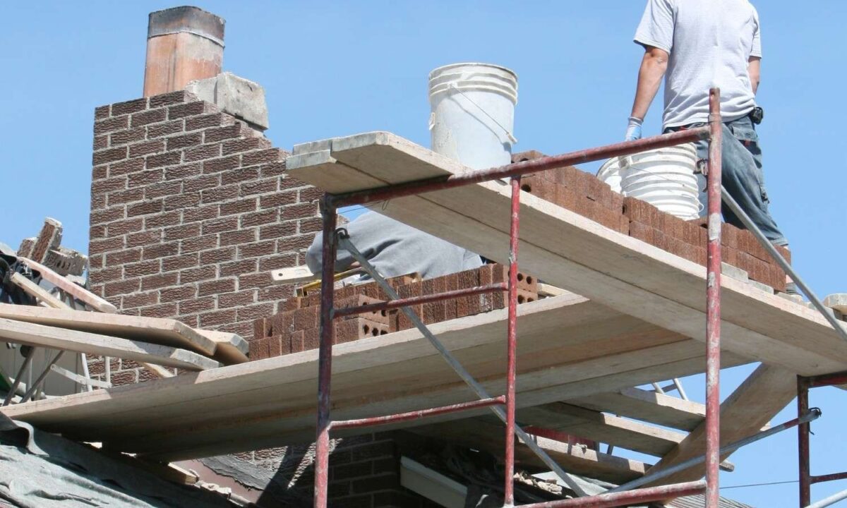 Chimney brickwork being rebuilt from scaffold planks with mortar buckets close by