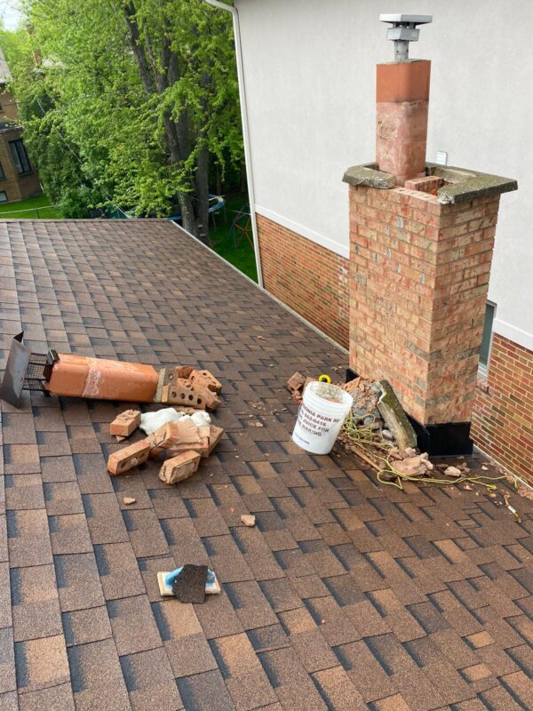 Tall brick chimney with a capped flue and salvaged bricks piled on the roof