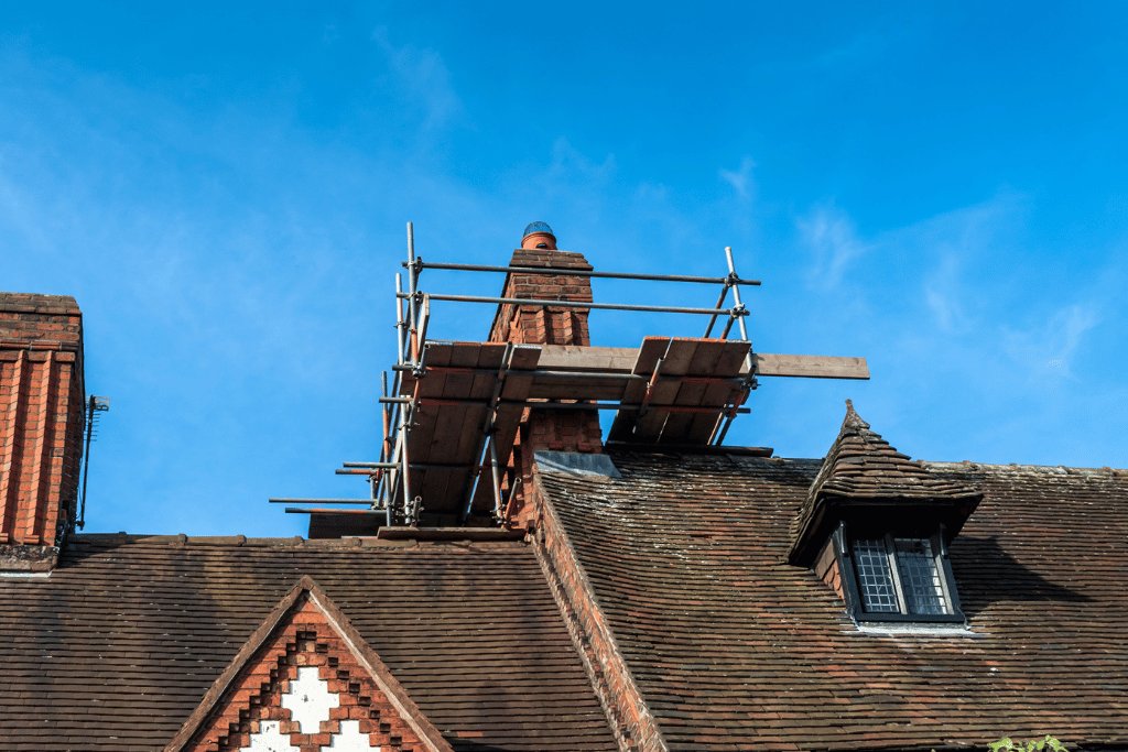 Scaffolding around a chimney stack on an old tiled roof with a dormer window