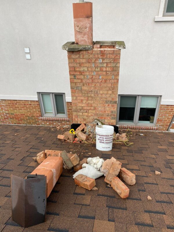 Brick chimney stack with rubble and an old flue liner scattered across roof shingles