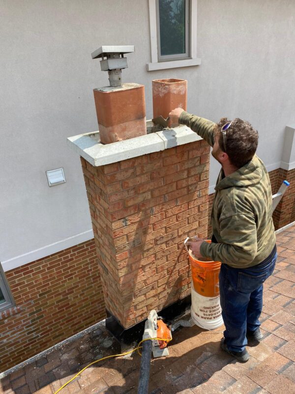 Mason packing mortar around clay flue liners while rebuilding a brick chimney crown