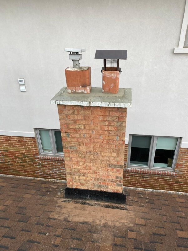 Finished brick chimney with two flue caps and a concrete crown above a stucco wall