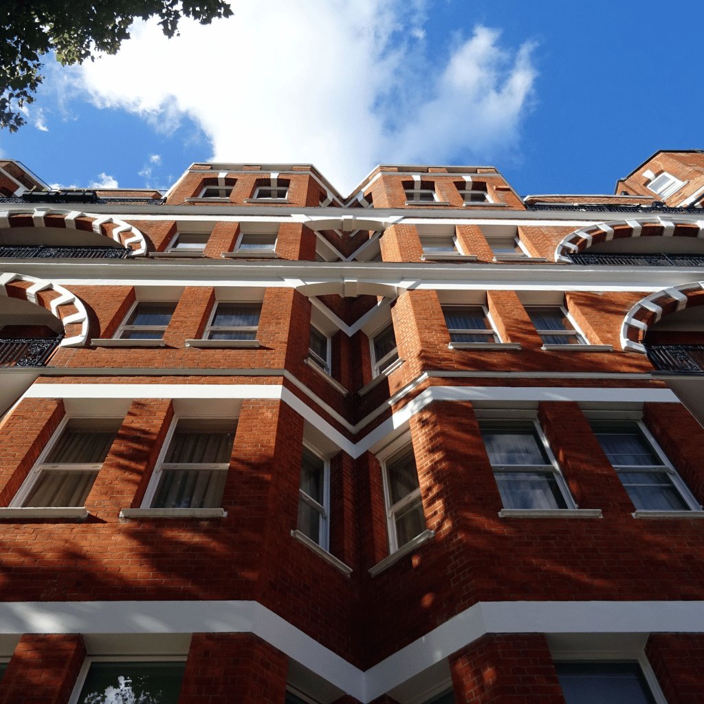 Looking up at a red brick building with white stone banding and many windows
