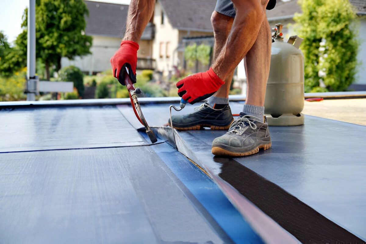 Roofer in red gloves sealing a blue membrane seam on a flat roof